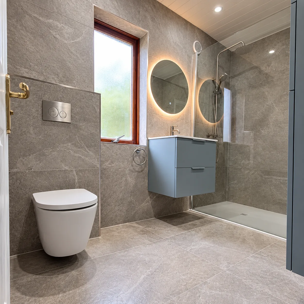 Grey stone-effect bathroom with wall-hung toilet, floating blue-grey vanity, illuminated round mirror and walk-in shower with rain head